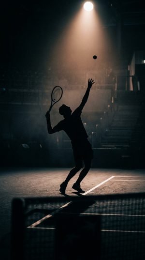 Silhouette of tennis player serving under stadium spotlight at night