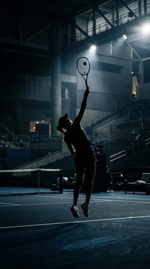 Silhouette of tennis player leaping for serve on illuminated court